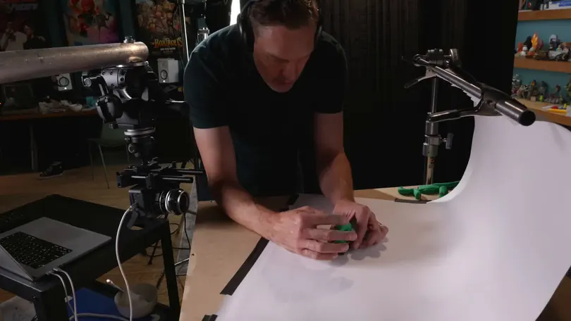 Andy Bailey, in headphones, poses a green clay figure on a white sweep in front of a camera rig