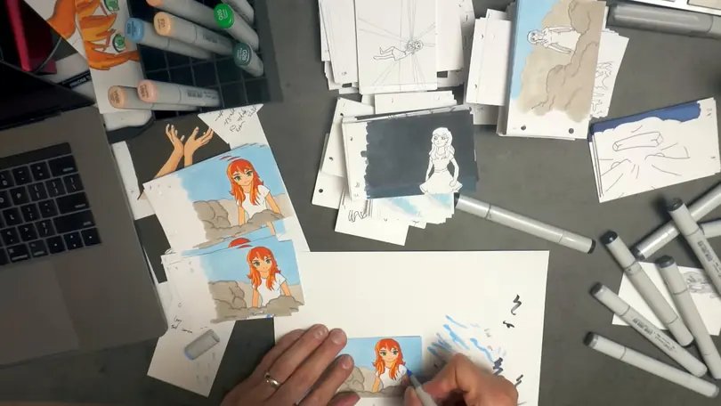 Overhead view of a desk covered in flipbook pages and markers, a hand coloring an anime frame