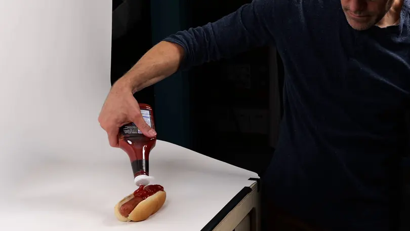 Andy Bailey squeezes ketchup onto a hot dog on a white sweep, shooting a close-up of the prop