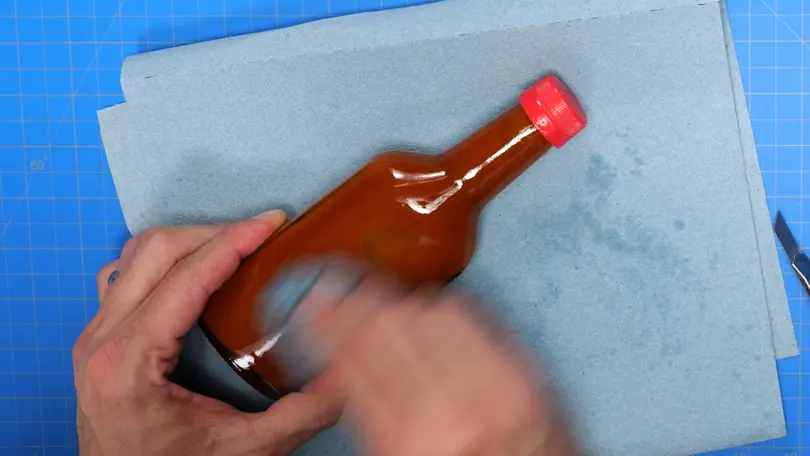 Hands paint a prop sauce bottle red and orange on a blue cutting mat