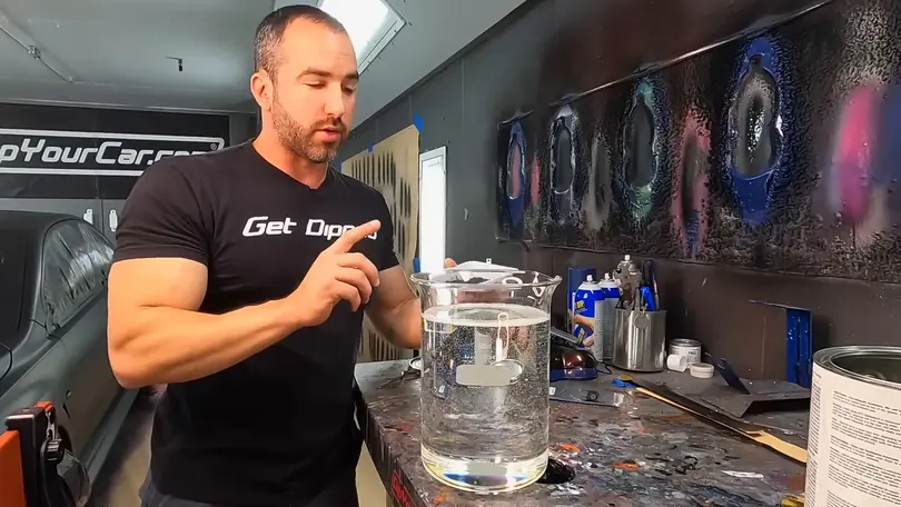 A presenter in a Get Dipped T-shirt holds up a beaker of clear liquid at the DipYourCar mixing bench