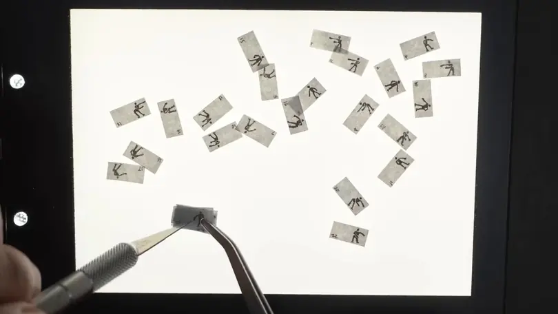 Tweezers and a craft knife stack tiny numbered flipbook pages of a dancing figure on a light box