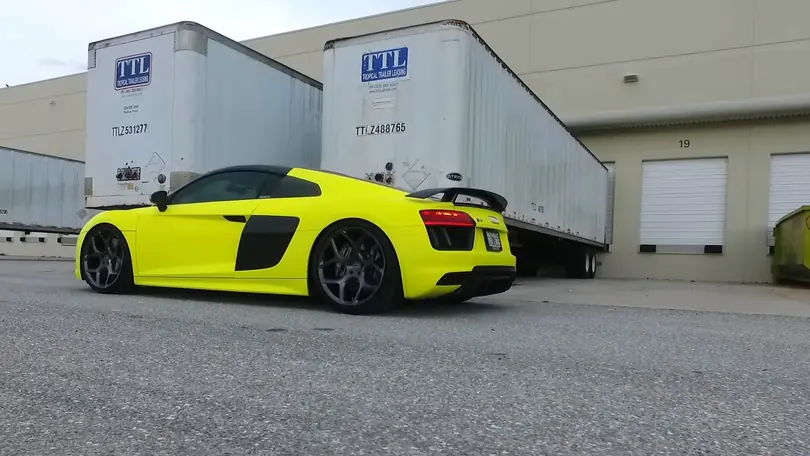 An Audi R8 in neon yellow parked low in front of trailers at a loading dock